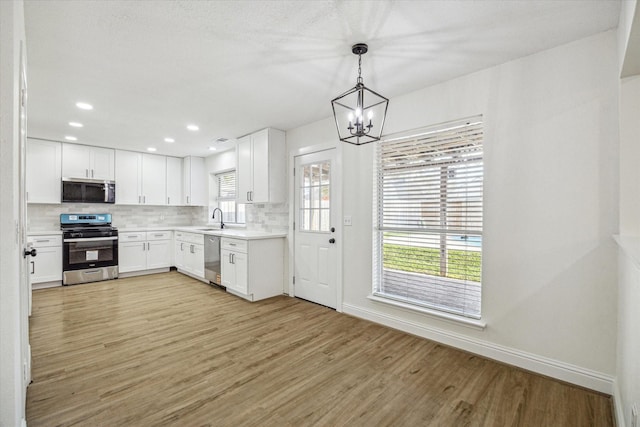 kitchen featuring light wood-type flooring, a sink, tasteful backsplash, appliances with stainless steel finishes, and a chandelier