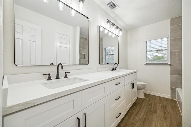 full bath with toilet, wood finished floors, visible vents, and a sink