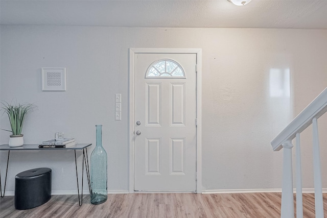 foyer featuring wood finished floors, baseboards, and stairway