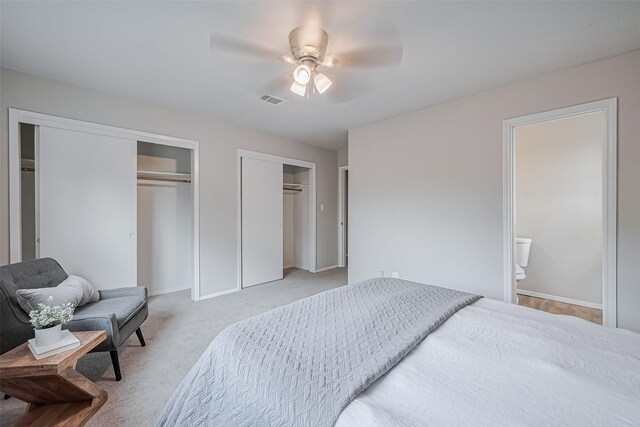 bedroom featuring baseboards, light carpet, two closets, visible vents, and ceiling fan