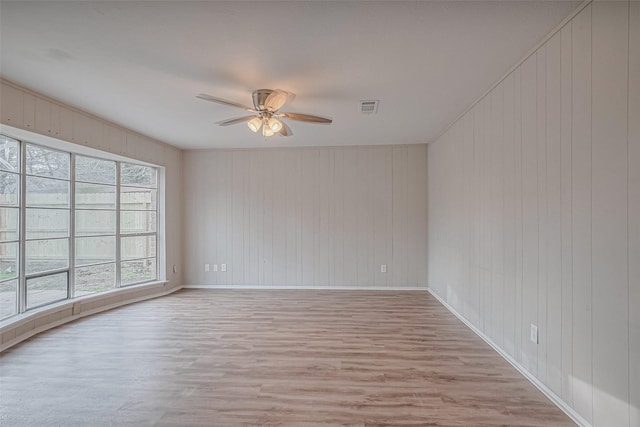 spare room featuring wood finished floors, ceiling fan, baseboards, and visible vents