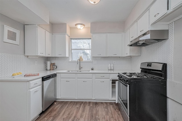 kitchen with appliances with stainless steel finishes, under cabinet range hood, light countertops, a sink, and light wood finished floors