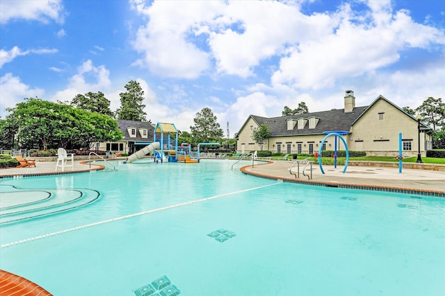 community pool with playground community, a water slide, a water play area, and a patio