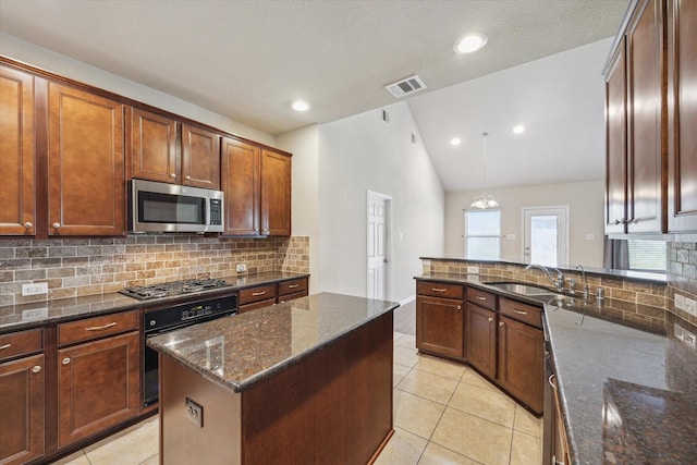 kitchen with lofted ceiling, light tile patterned floors, dark stone countertops, appliances with stainless steel finishes, and a sink