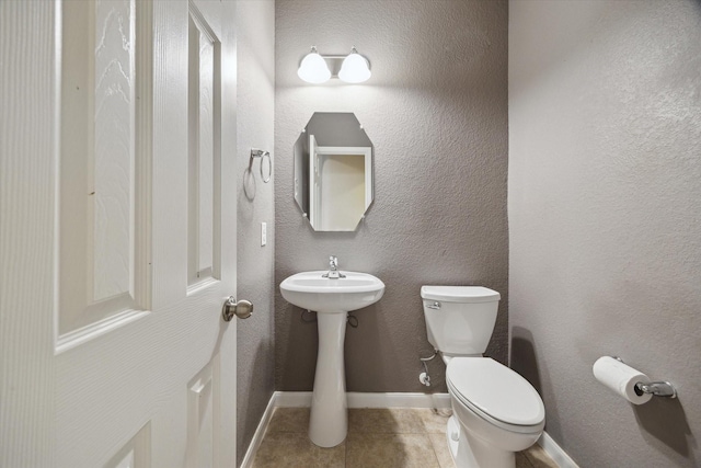 bathroom featuring tile patterned flooring, toilet, baseboards, and a textured wall