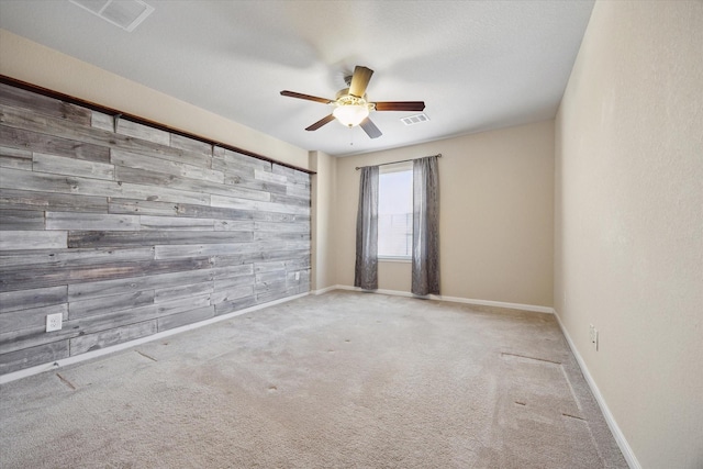 unfurnished room featuring baseboards, visible vents, ceiling fan, wood walls, and carpet flooring