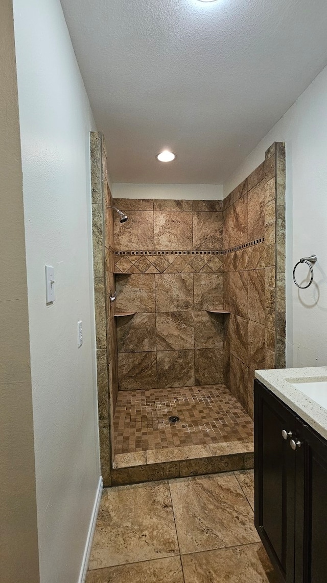 full bath featuring vanity, baseboards, a tile shower, and a textured ceiling