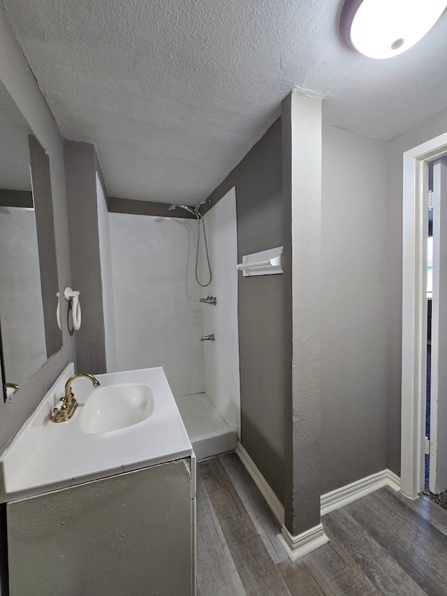 full bathroom with a textured ceiling, walk in shower, baseboards, wood finished floors, and vanity