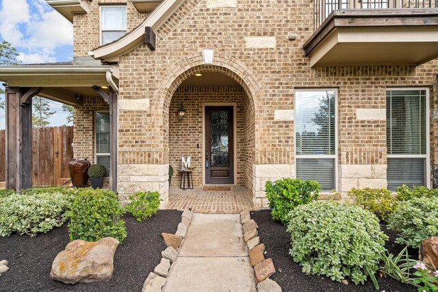 doorway to property with brick siding, fence, and a balcony