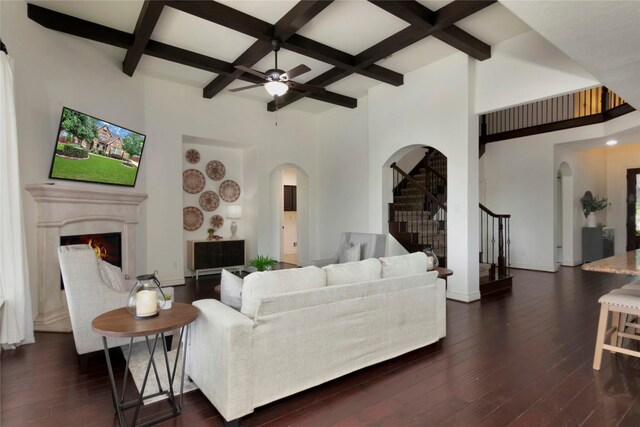 living room featuring beam ceiling, arched walkways, stairs, a ceiling fan, and coffered ceiling