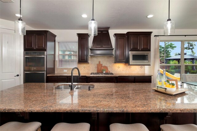 kitchen with a sink, appliances with stainless steel finishes, a breakfast bar, and custom range hood