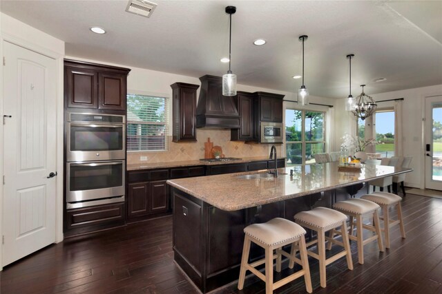 kitchen with dark wood-style flooring, visible vents, a sink, custom exhaust hood, and stainless steel appliances