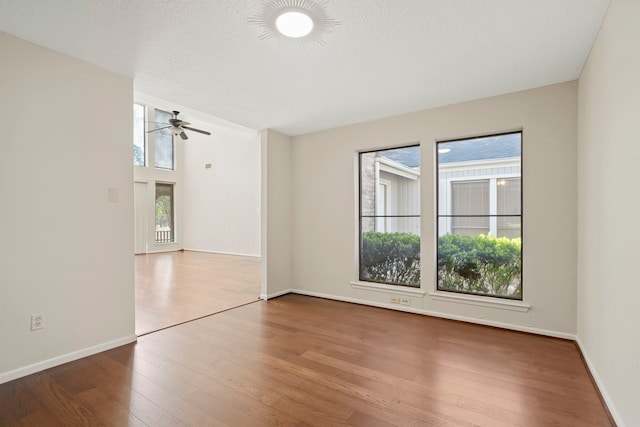 empty room with wood finished floors, baseboards, a wealth of natural light, and ceiling fan