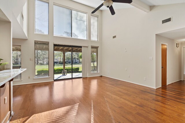 unfurnished living room featuring wood finished floors, baseboards, visible vents, beam ceiling, and ceiling fan