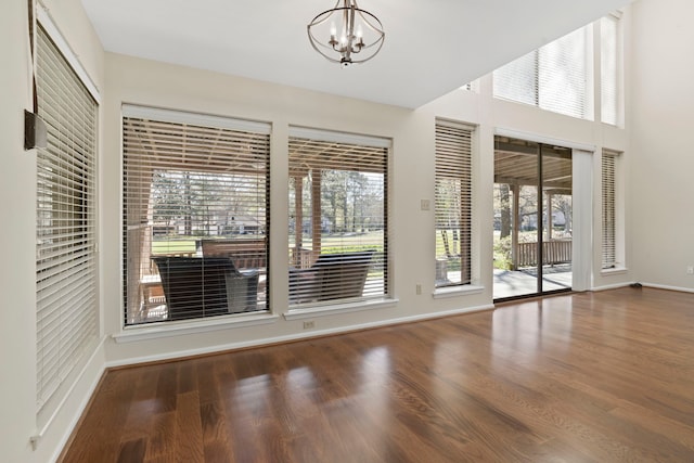 empty room featuring an inviting chandelier, wood finished floors, and baseboards