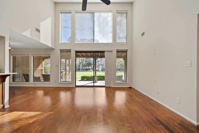 unfurnished living room with wood finished floors, baseboards, visible vents, ceiling fan, and a towering ceiling