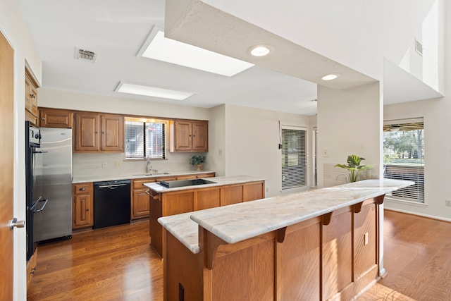 kitchen with a kitchen bar, light wood-type flooring, black appliances, a sink, and a center island