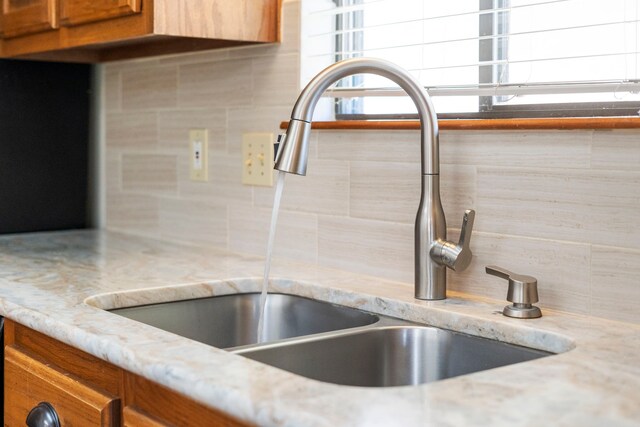 details featuring brown cabinetry, tasteful backsplash, light stone countertops, and a sink