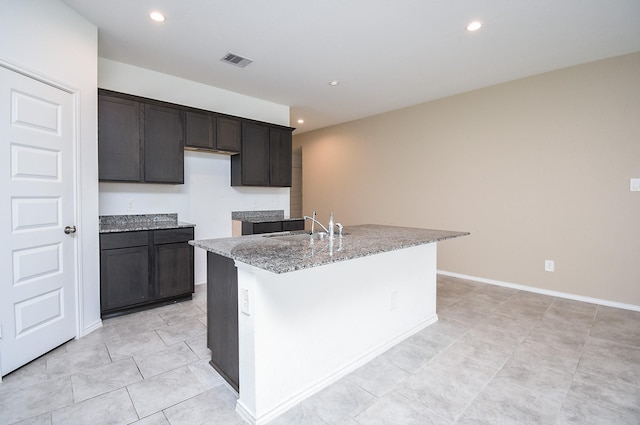 kitchen featuring visible vents, light stone countertops, a center island with sink, recessed lighting, and a sink