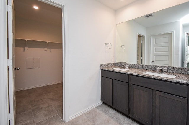 bathroom with double vanity, visible vents, a walk in closet, and a sink