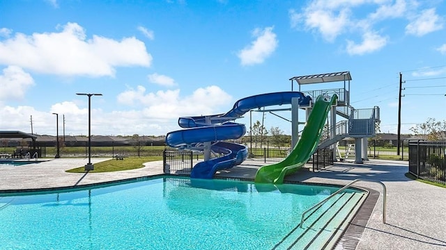 community pool with playground community, a water slide, and fence