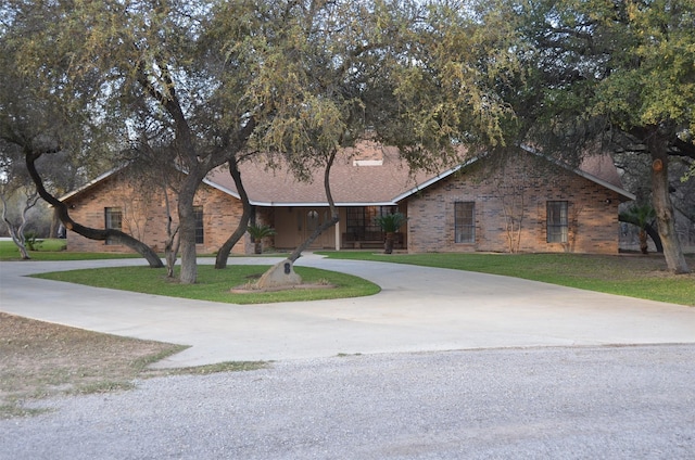 ranch-style home with brick siding, curved driveway, and a front lawn