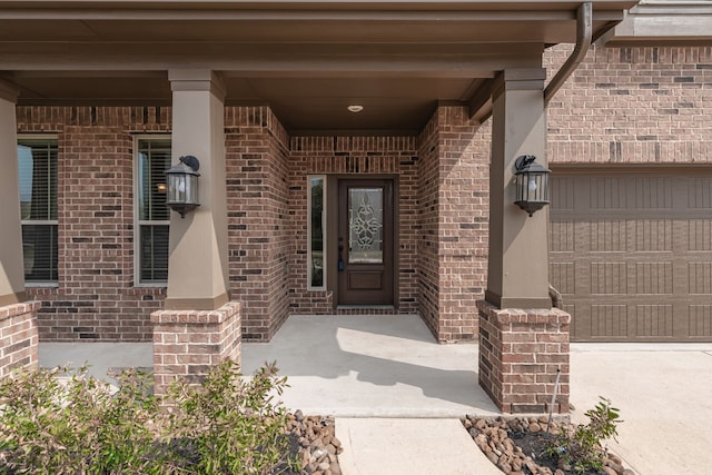 entrance to property featuring a porch, a garage, brick siding, and driveway