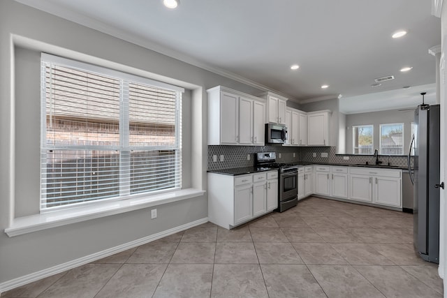 kitchen with dark countertops, backsplash, crown molding, appliances with stainless steel finishes, and white cabinets