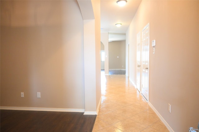 hallway featuring light tile patterned floors, baseboards, and arched walkways