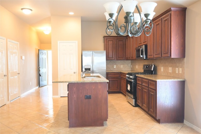 kitchen featuring a center island with sink, light stone counters, backsplash, stainless steel appliances, and an inviting chandelier