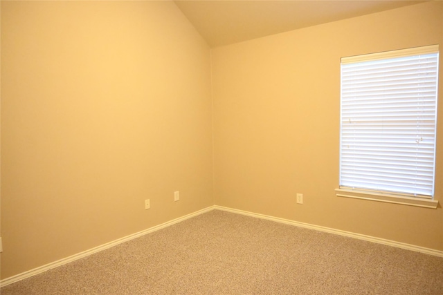 carpeted spare room featuring baseboards and vaulted ceiling