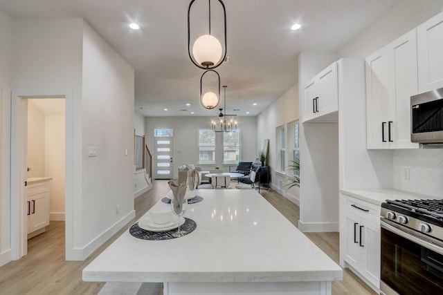 kitchen with a kitchen island, stainless steel appliances, light wood-style floors, white cabinetry, and backsplash