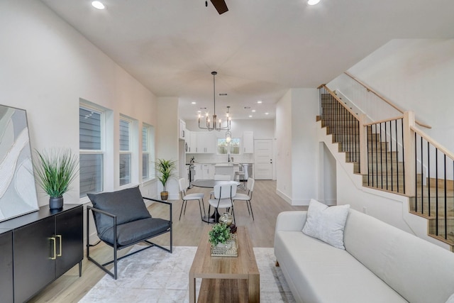 living room with baseboards, stairs, recessed lighting, light wood-style flooring, and ceiling fan with notable chandelier