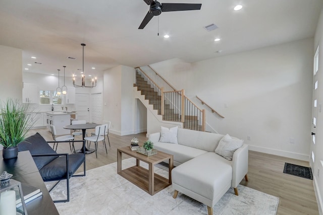 living area featuring visible vents, light wood-type flooring, stairs, recessed lighting, and ceiling fan with notable chandelier