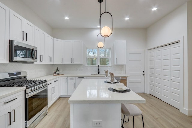 kitchen with a sink, a kitchen island, appliances with stainless steel finishes, and light wood finished floors