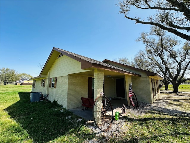 view of side of home with a patio, a lawn, brick siding, and central AC