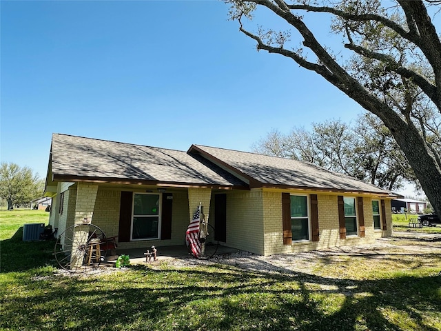 view of front of home featuring a front lawn, central AC unit, brick siding, and roof with shingles