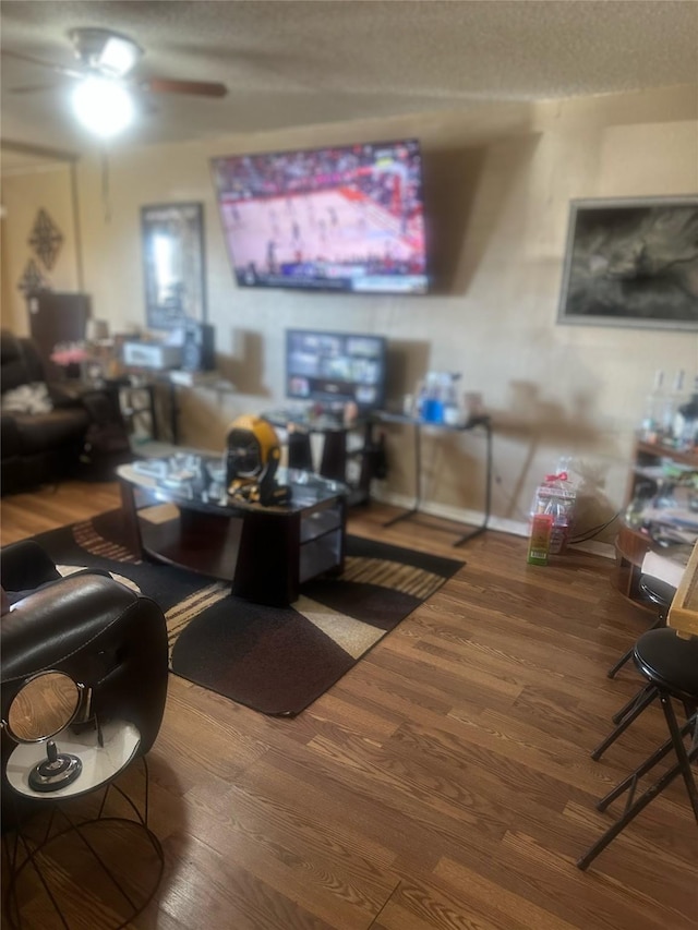 living area featuring a ceiling fan, wood finished floors, baseboards, and a textured ceiling