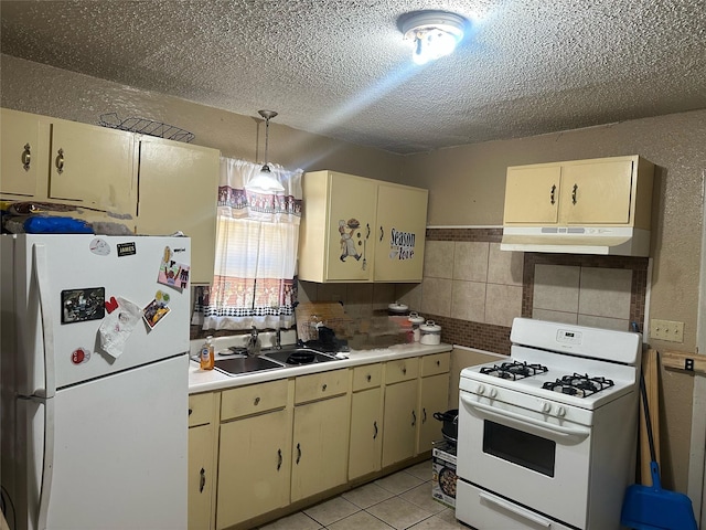 kitchen with under cabinet range hood, light tile patterned floors, cream cabinets, white appliances, and a sink