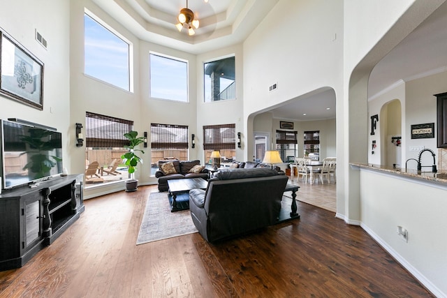 living area featuring visible vents, wood-type flooring, a towering ceiling, baseboards, and arched walkways