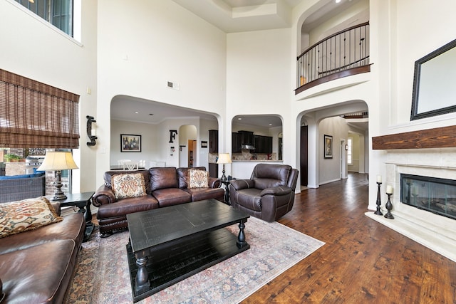 living area with visible vents, arched walkways, a high ceiling, and wood finished floors