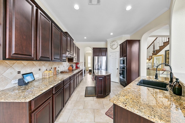 kitchen with light stone counters, arched walkways, a sink, and stainless steel appliances