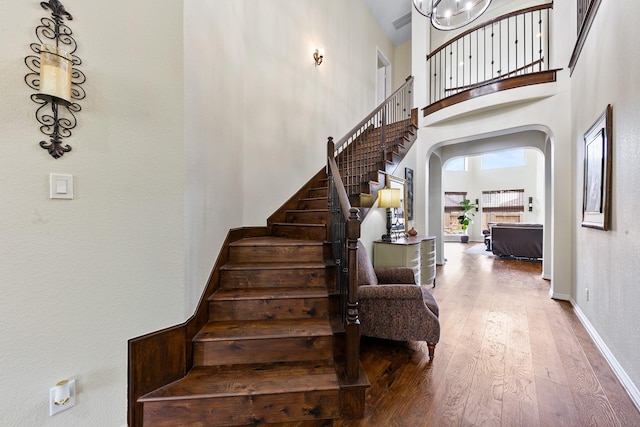 staircase with wood-type flooring, arched walkways, baseboards, and a towering ceiling