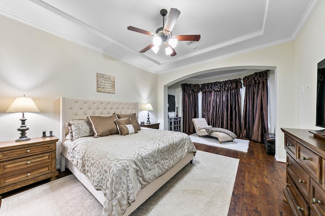 bedroom with ceiling fan, arched walkways, wood finished floors, a tray ceiling, and ornamental molding
