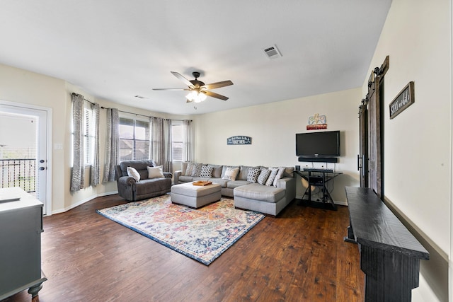 living room with visible vents, baseboards, dark wood-style floors, a barn door, and a ceiling fan