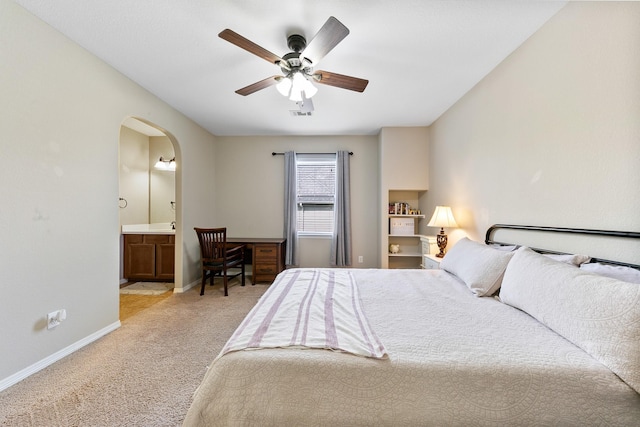 bedroom with ceiling fan, light carpet, arched walkways, baseboards, and ensuite bathroom