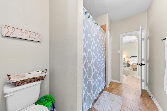 ensuite bathroom with tile patterned floors, baseboards, toilet, and ensuite bath
