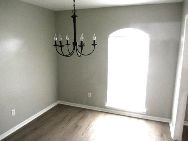 unfurnished dining area with an inviting chandelier, wood finished floors, and baseboards