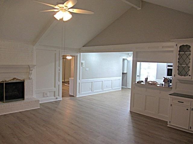 unfurnished living room featuring wood finished floors, a decorative wall, a fireplace, and ceiling fan