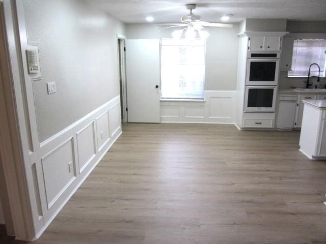 unfurnished dining area with a decorative wall, light wood-style flooring, a ceiling fan, and a sink